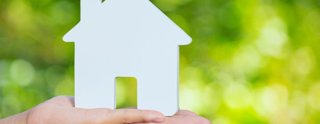 緑を背景に家の模型を持つ手